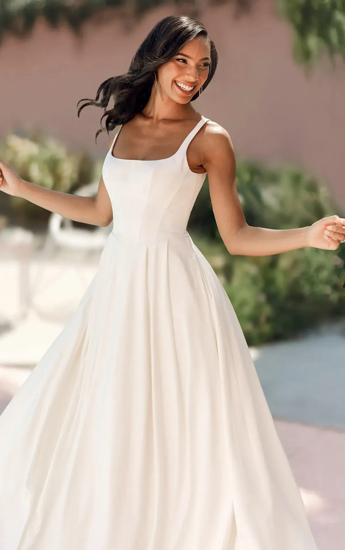 A woman is wearing a white dress and smiling while twirling outdoors.